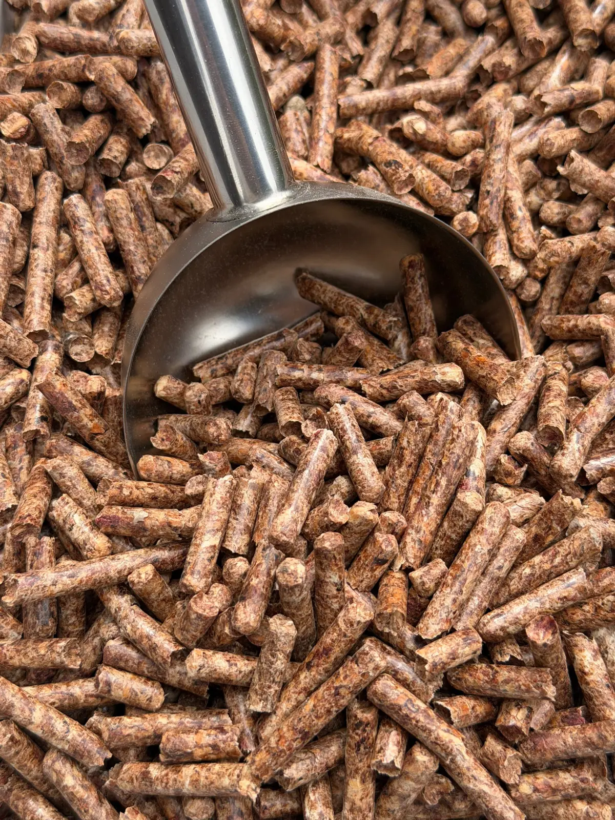 Nahaufnahme brauner Holzpellets mit einer Metallschaufel.